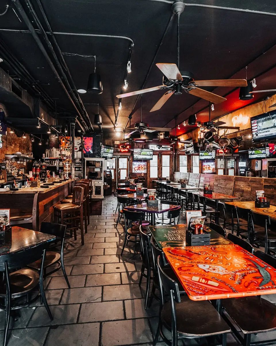 The long Main Dining Room at Olde Nola Cookery: painted tabletops, black chairs, ceiling fans and the bar running along the right