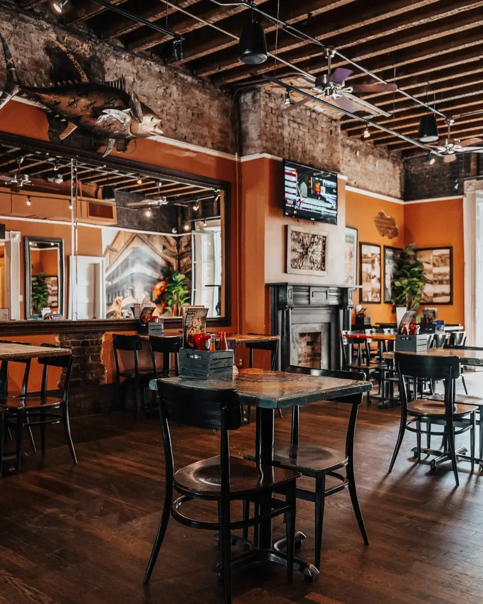 The Royal Room: orange walls, exposed wood beams, tall mirrors and a mounted fish above the fireplace