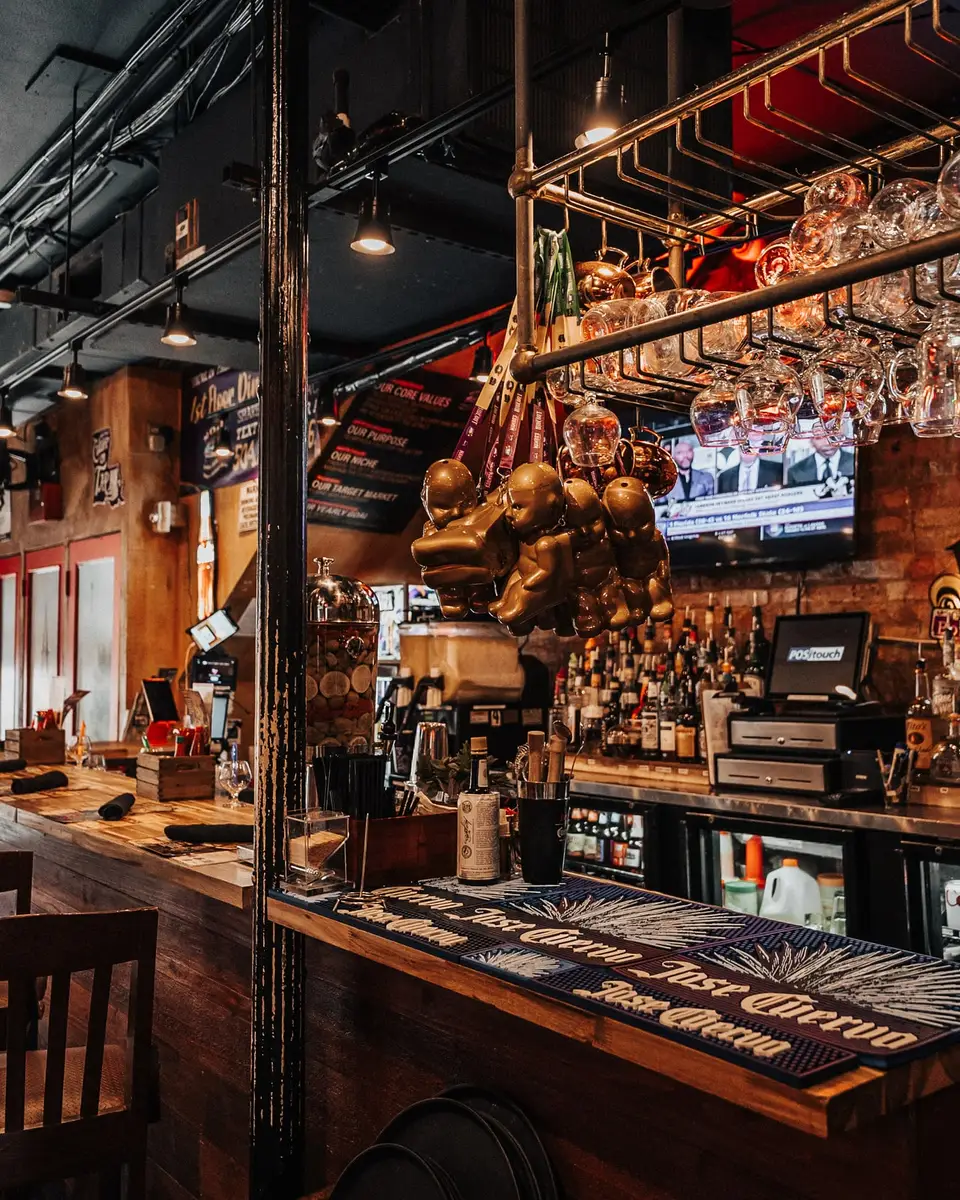 The main bar under a rack of hanging copper pots, with exposed brick and a lit liquor wall