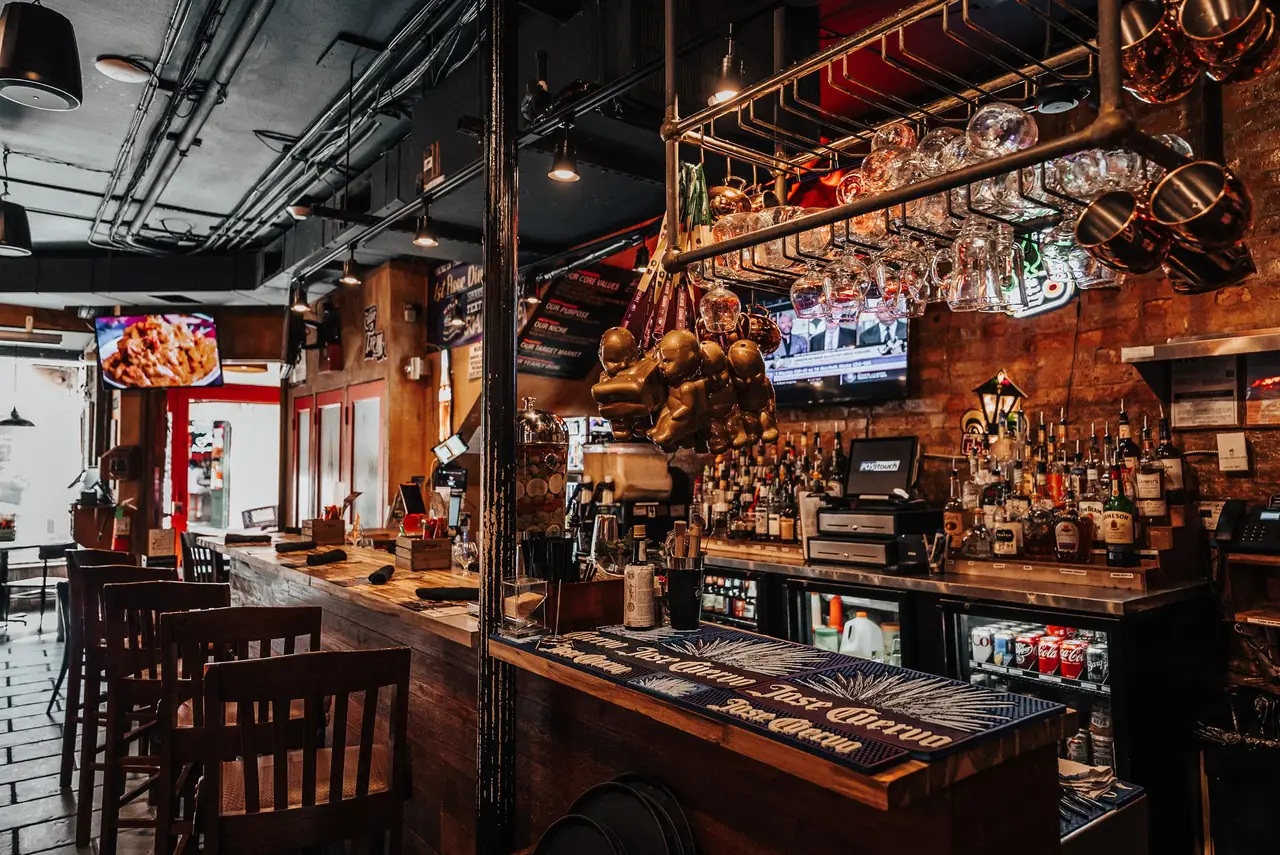 The main bar under a rack of hanging copper pots, with exposed brick and a lit liquor wall