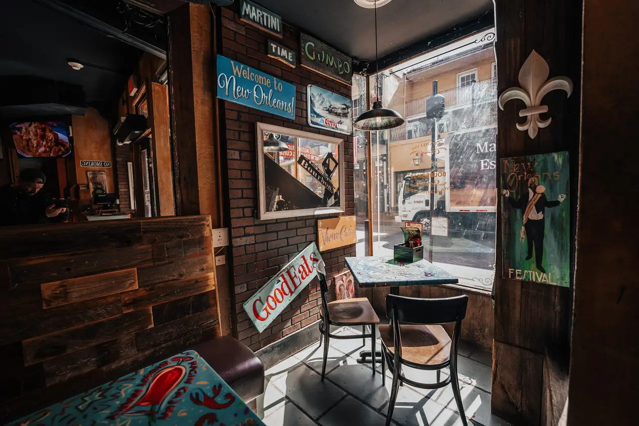 Corner window table by a “Welcome to New Orleans” sign, with a street view through the glass