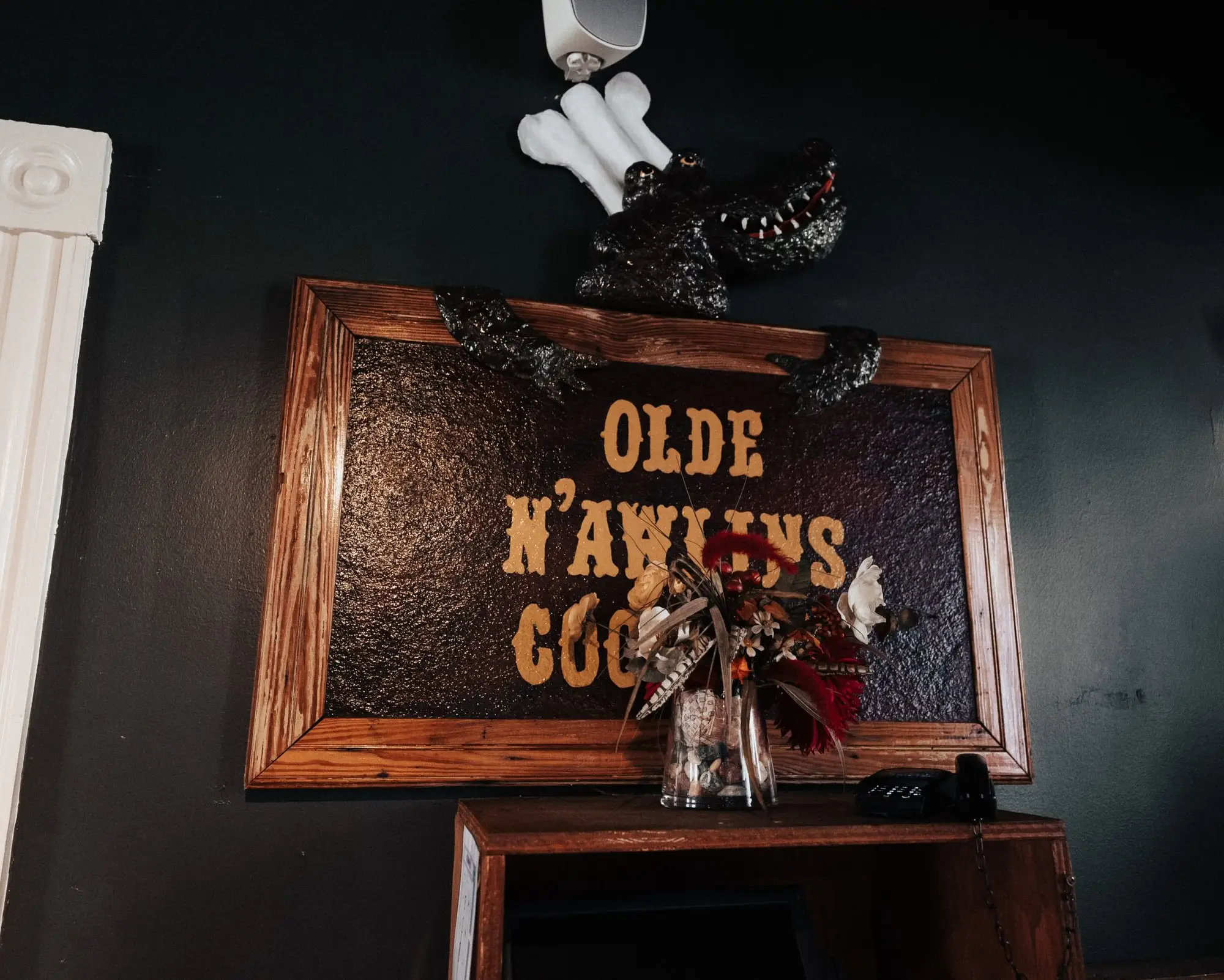 Carved “Olde N’awlins Cookery” wooden sign hung with beads in the Mardi Gras Room