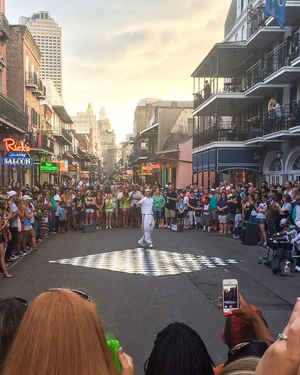 A crowd gathered around a street performance on Bourbon Street under the balconies