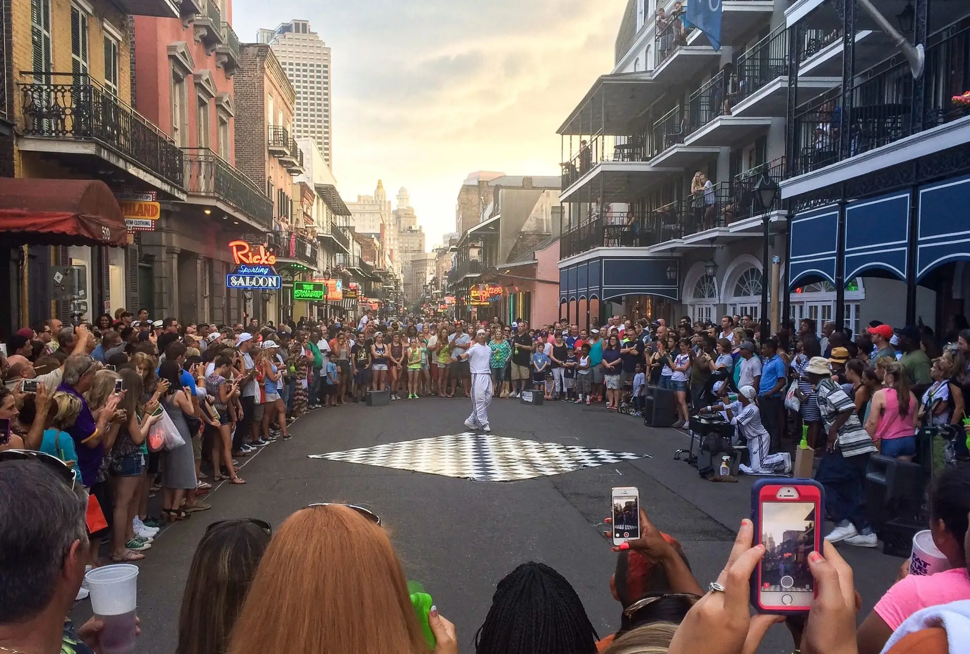 A crowd gathered around a street performance on Bourbon Street under the balconies